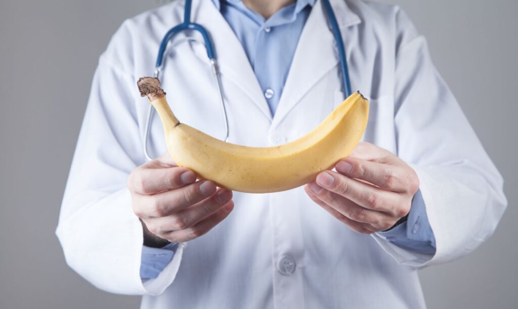 Médico segura banana simbolizando implante peniano Médico segura banana simbolizando implante peniano.