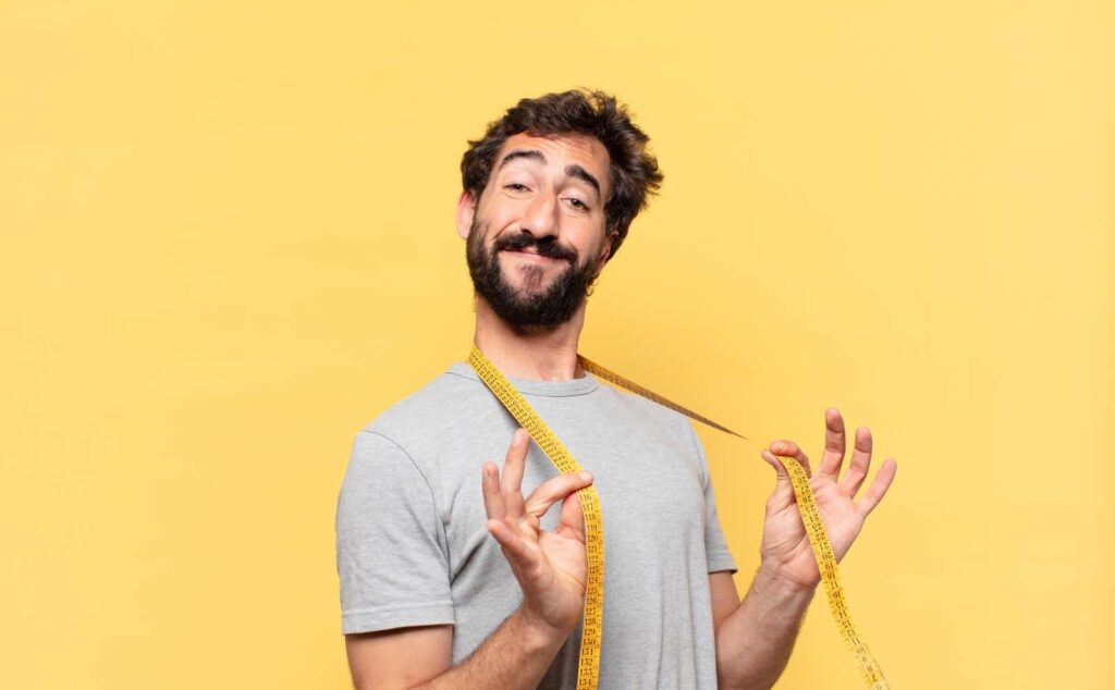 Homem confiante com fita métrica no ombro representa autoestima após tratamento com aumentador peniano.