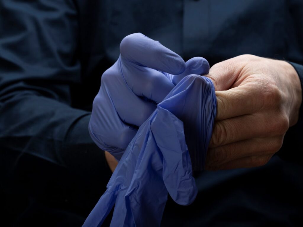Pessoa colocando luva cirúrgica azul, representando os preparativos para cirurgia de aumento peniano com foco em segurança e técnica.