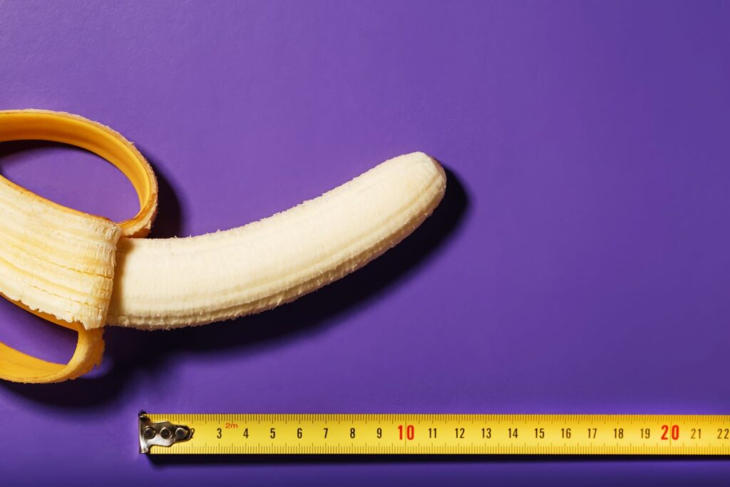 Tamanho do pênis: será que o seu está na média? Banana parcialmente descascada com fita métrica, ilustrando o tema do tamanho do pênis de forma simbólica e didática.