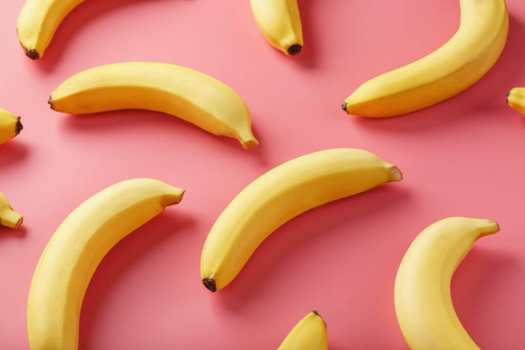 Composição com várias bananas amarelas dispostas em diferentes posições e curvaturas sobre fundo rosa, formando um padrão visual associado simbolicamente a variações de formato.