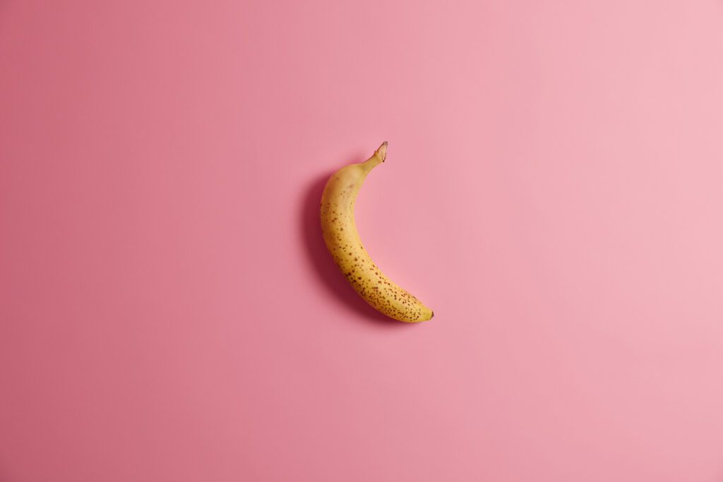 Banana amarela curvada sobre fundo rosa, utilizada como ilustração para o tema preenchimento peniano em casos de pênis fino.