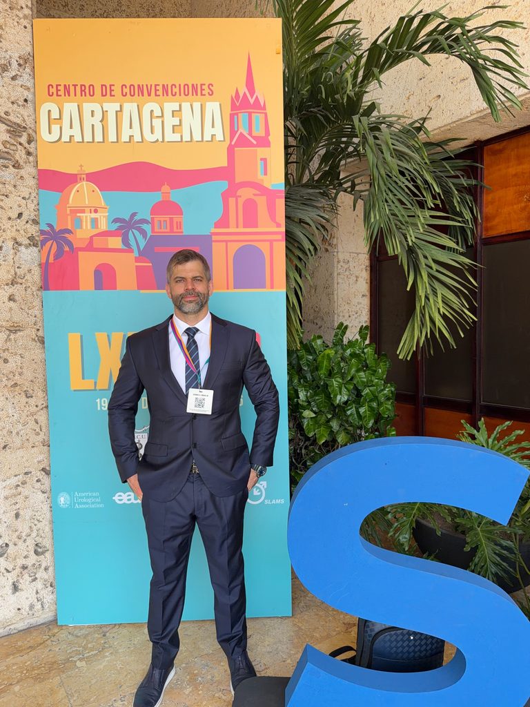 Dr. Marco Túlio Cavalcanti posa de terno e crachá diante de painel do Centro de Convenciones Cartagena durante o LXI Congresso Colombiano de Urologia.
