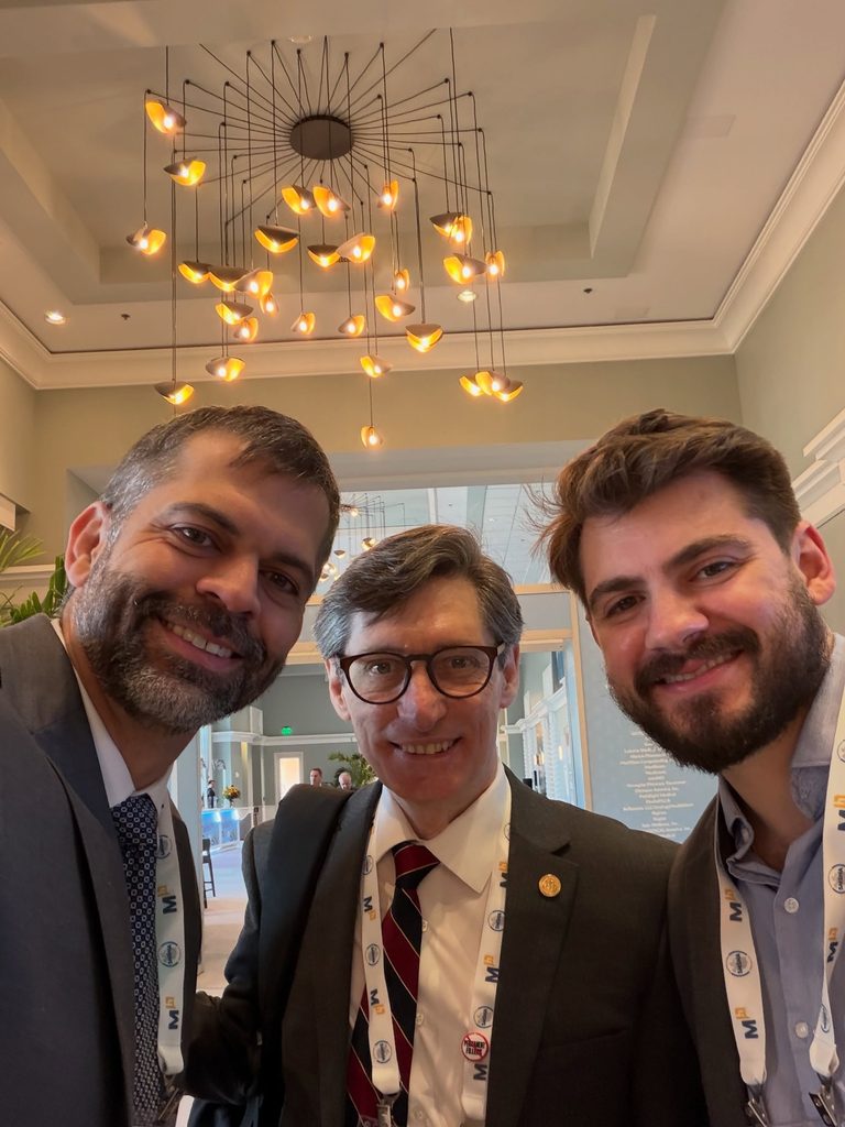 Por que a presença no SMSNA 2026 importa para o paciente? Dr. Marco Túlio Cavalcanti posa com dois colegas médicos durante congresso internacional, em registro de interação profissional e troca de experiências entre especialistas.